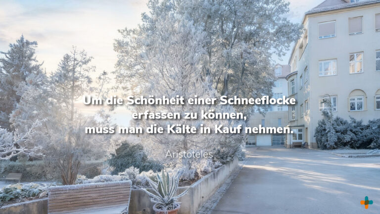Wintermotiv mit Raureif-Bäumen vor dem Klinikum-Gebäude. Das Aristoteles-Zitat über die Kälte und die Schönheit einer Schneeflocke ist eingeblendet.
