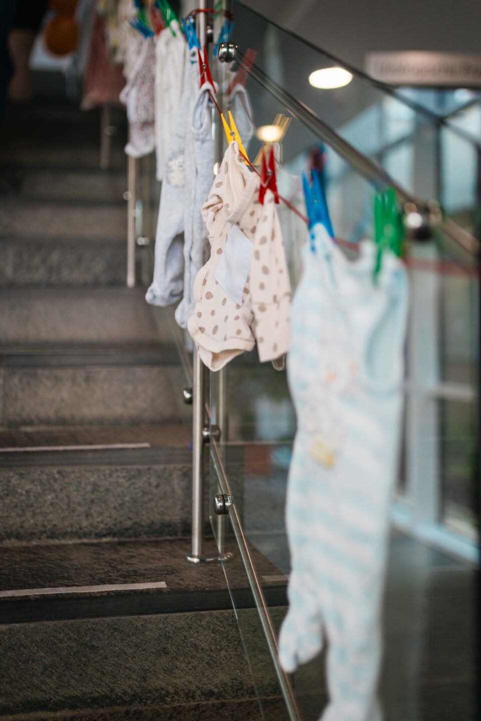 An einer Wäscheleine am Treppengeländer aufgehängte Babykleidung wie Strampler und Bodys.