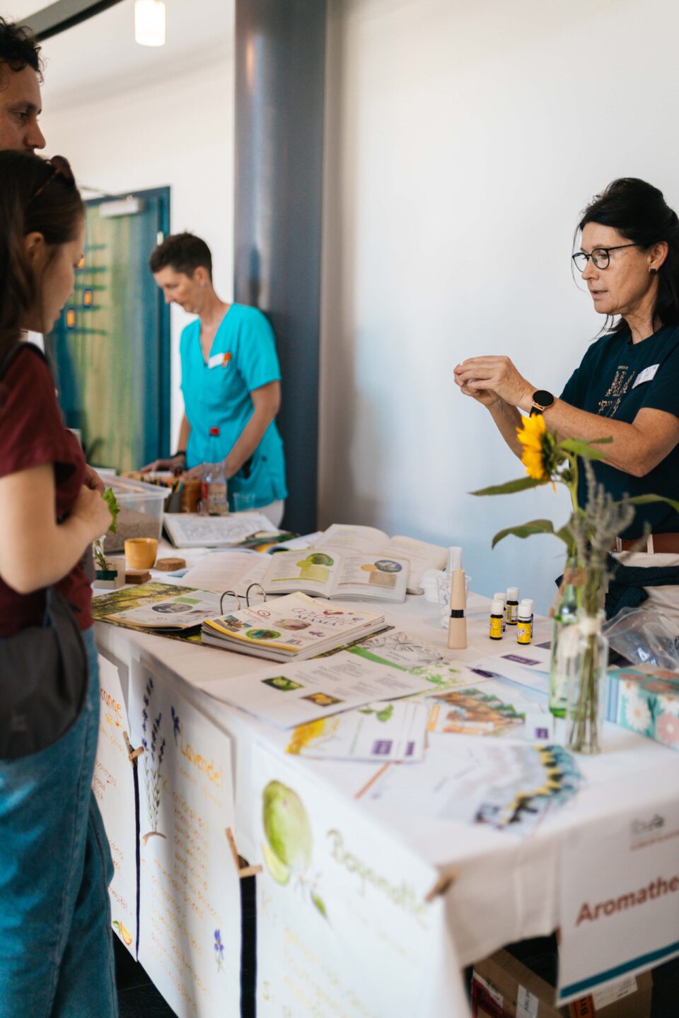 Eine Beraterin im Gespräch mit einer Besucherin an einem Infostand für Babytragen und Tragetücher im Flur.