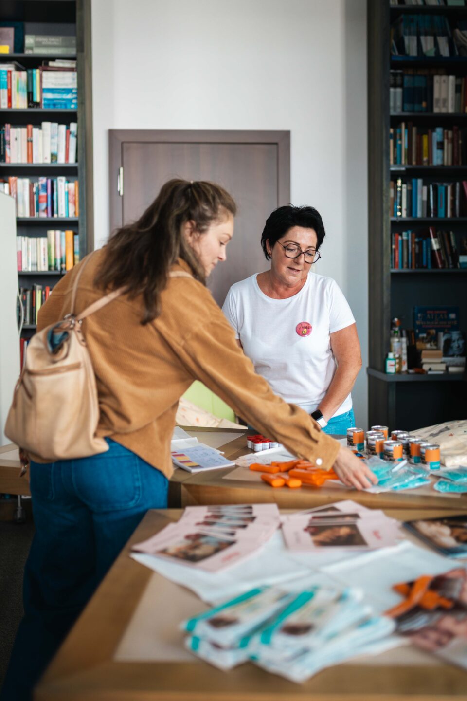 Junge Frau lässt sich an einem Informationsstand mit Flyern und Giveaways von einer Mitarbeiterin beraten.