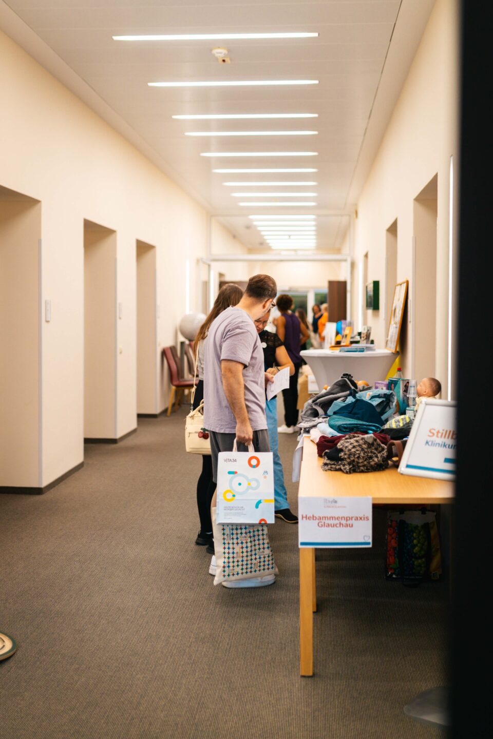 Werdende Eltern informieren sich am Stand der Hebammenpraxis Glauchau in einem hellen Flur.